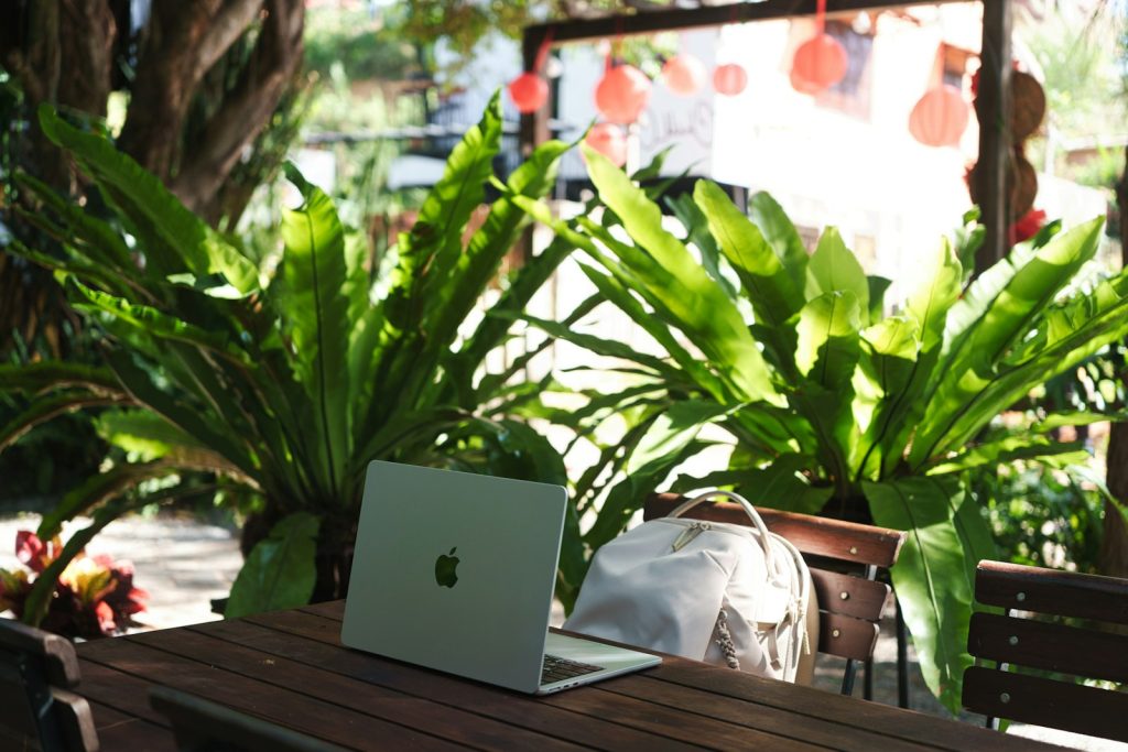 Laptop and backpack on a wooden table surrounded by plants.